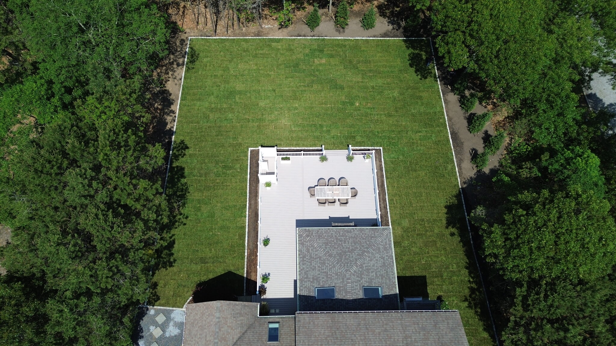 Aerial view of a newly sodded backyard with a white composite deck and outdoor dining area