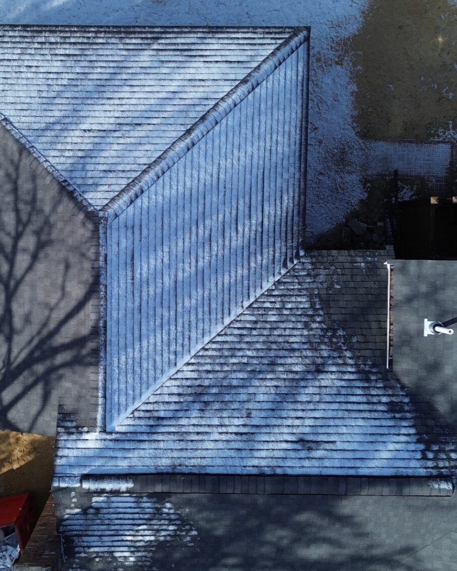 Aerial view of a completed asphalt shingle roof dusted with light snow