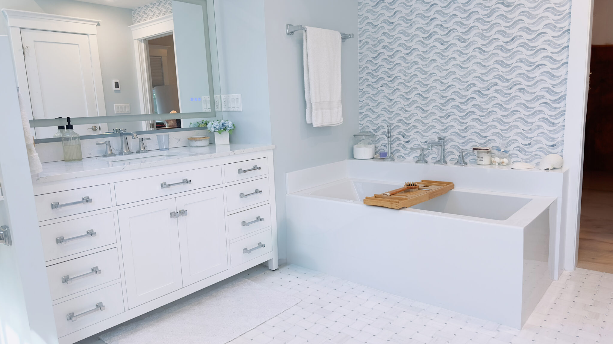 Remodeled bathroom with soaking tub, white vanity and wave-pattern tile accent wall