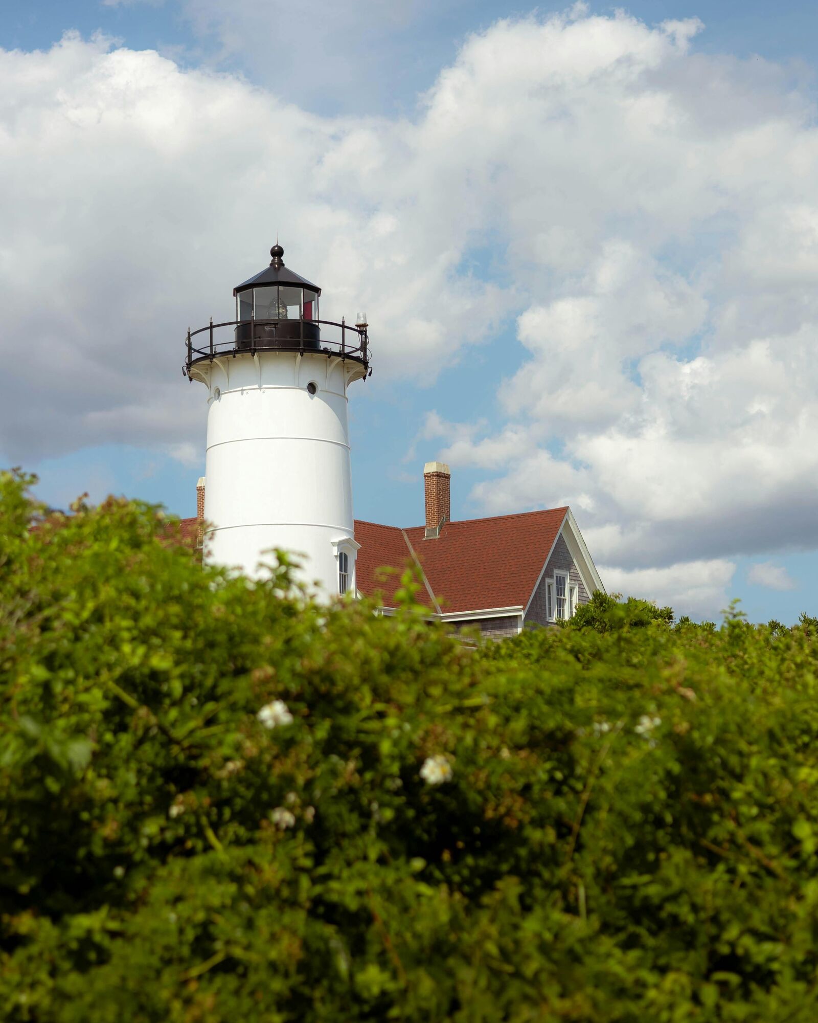 White lighthouse beside a red-roofed house on Cape Cod