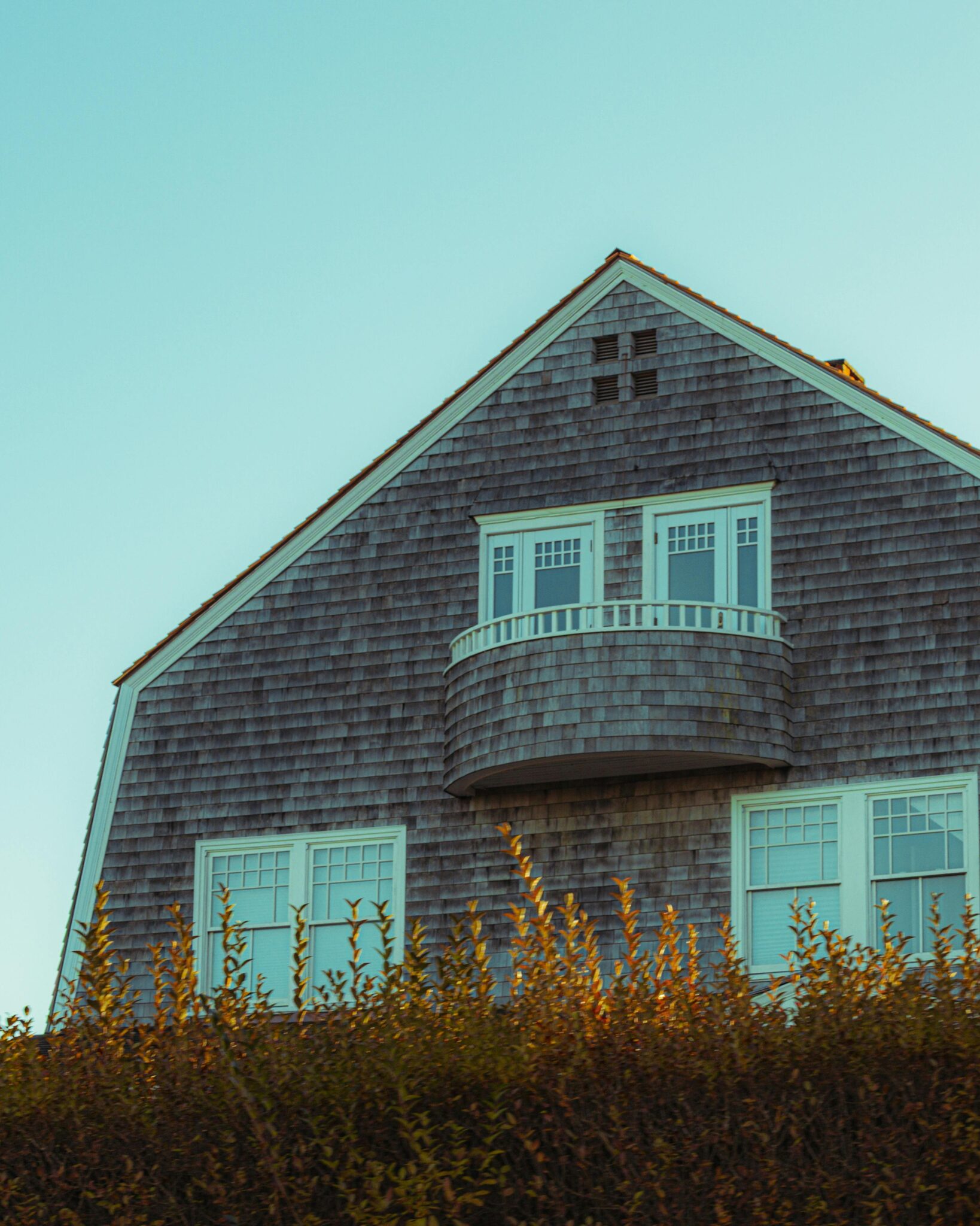 Weathered cedar-shingle Cape Cod home with a curved second-story balcony