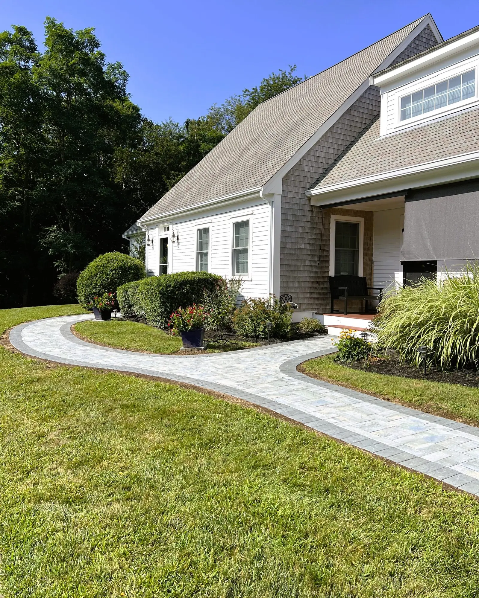 Curved paver walkway and landscaped planting beds in front of a Cape Cod home