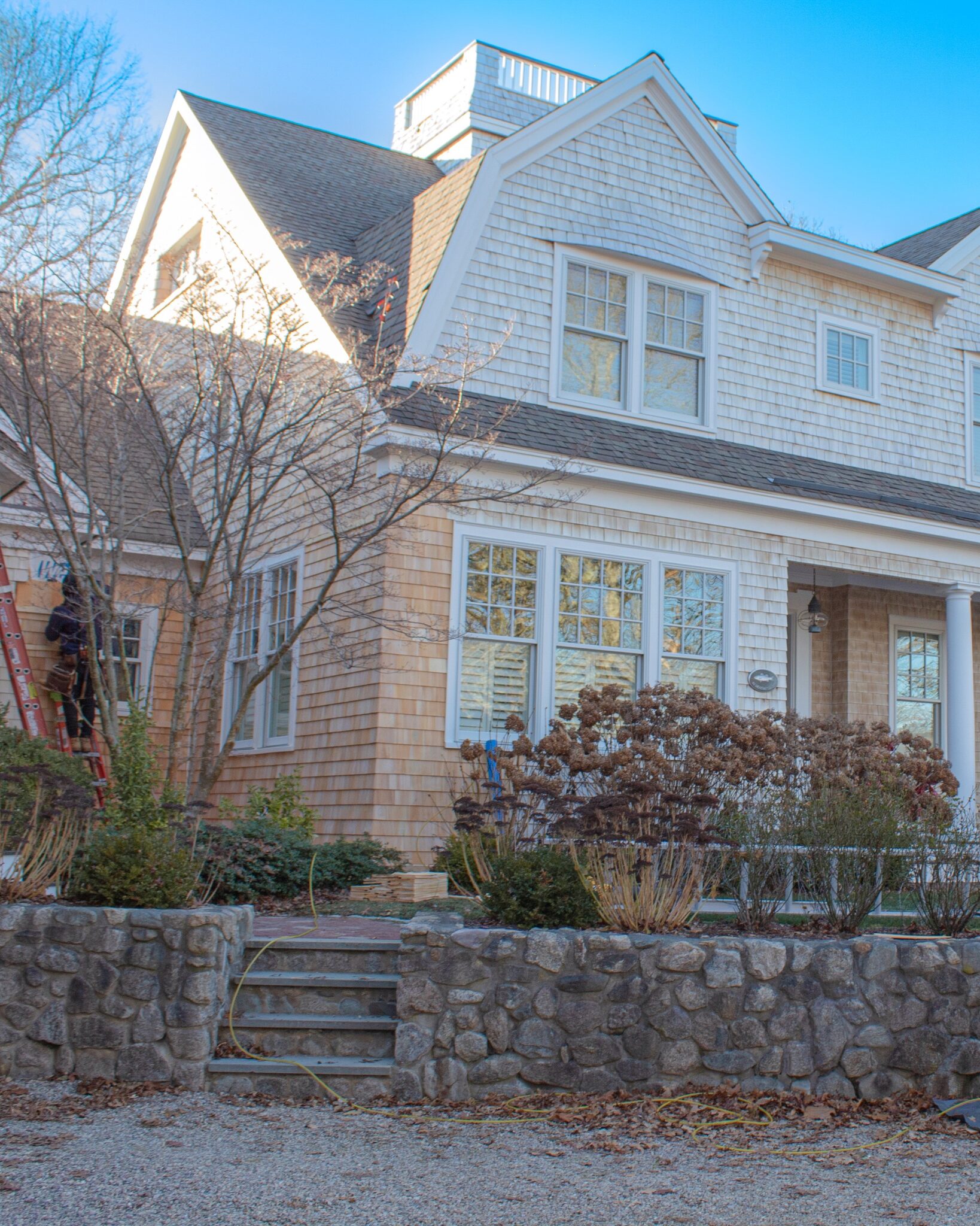 Shingle-style custom home with a fieldstone retaining wall during exterior finish work