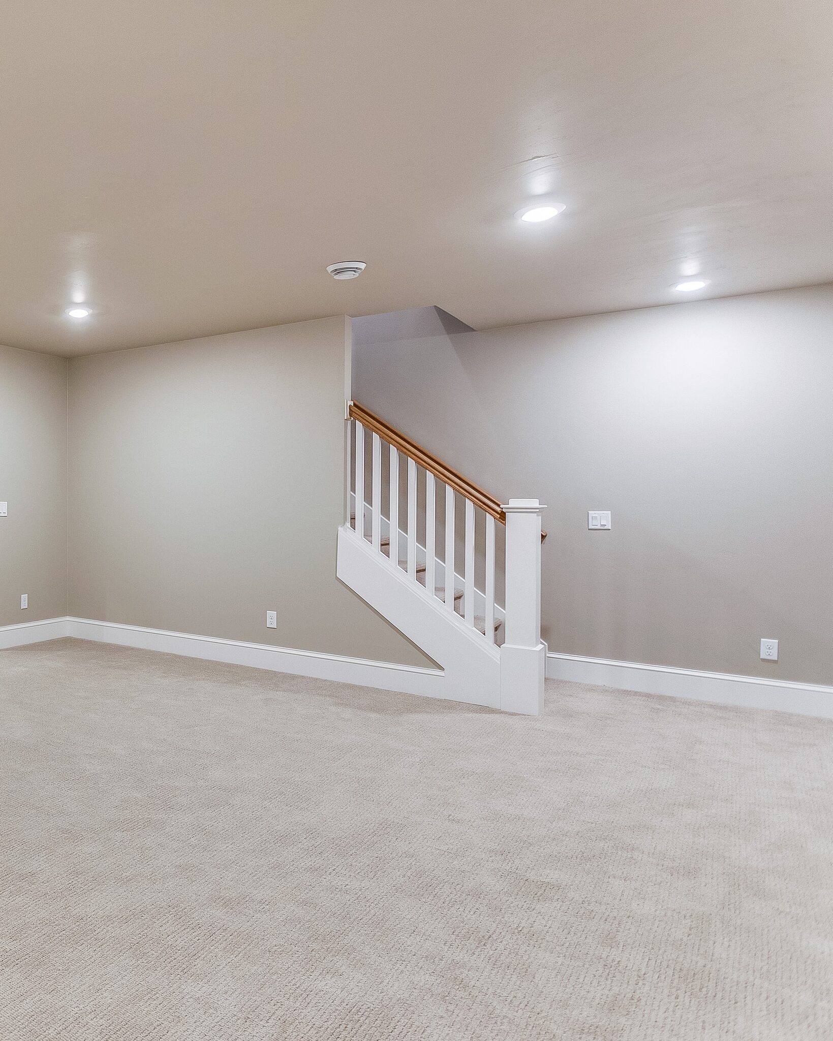 Finished basement with new carpet, painted walls and a wood stair railing