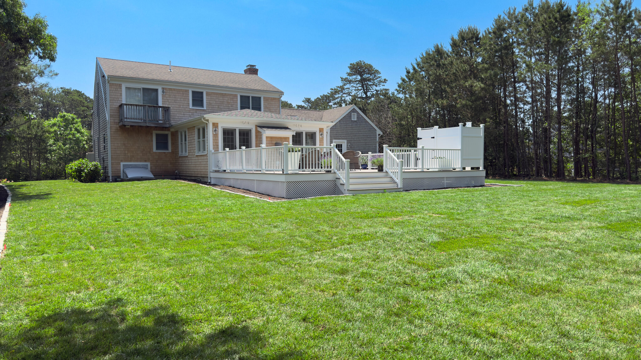 Rear deck with white railings on a Cape Cod home with a freshly graded lawn