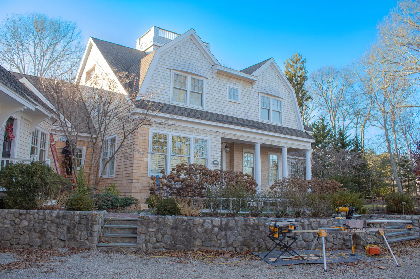 Cape Cod shingle-style home during exterior renovation with staging and ladders