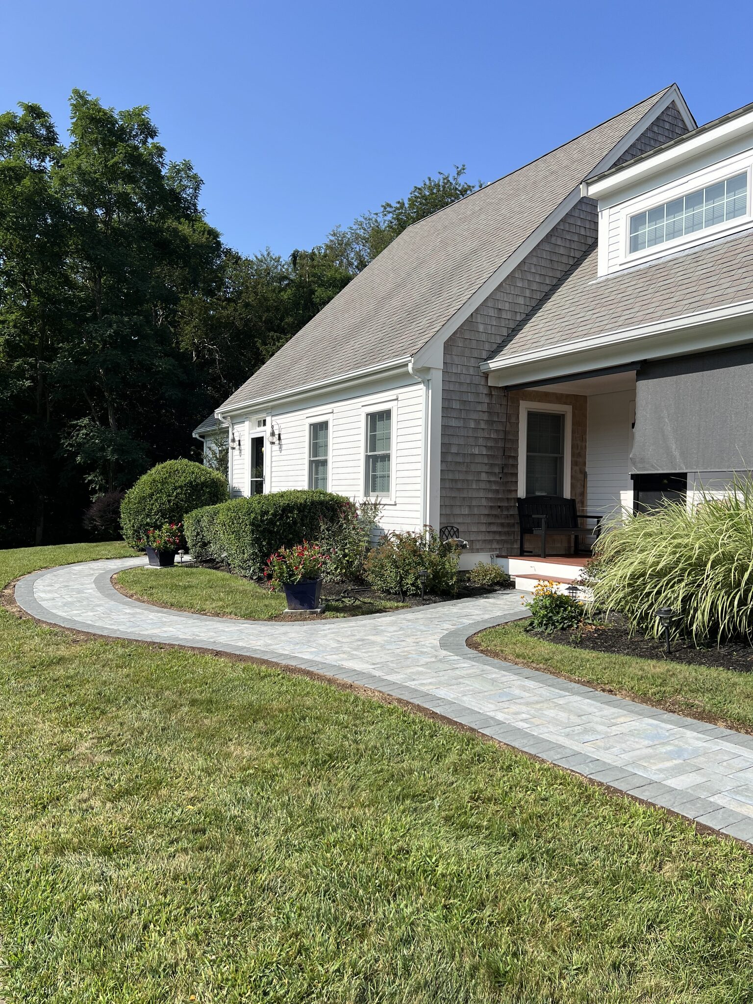 Stone-bordered paver walkway leading to the front entry of a shingled cape home